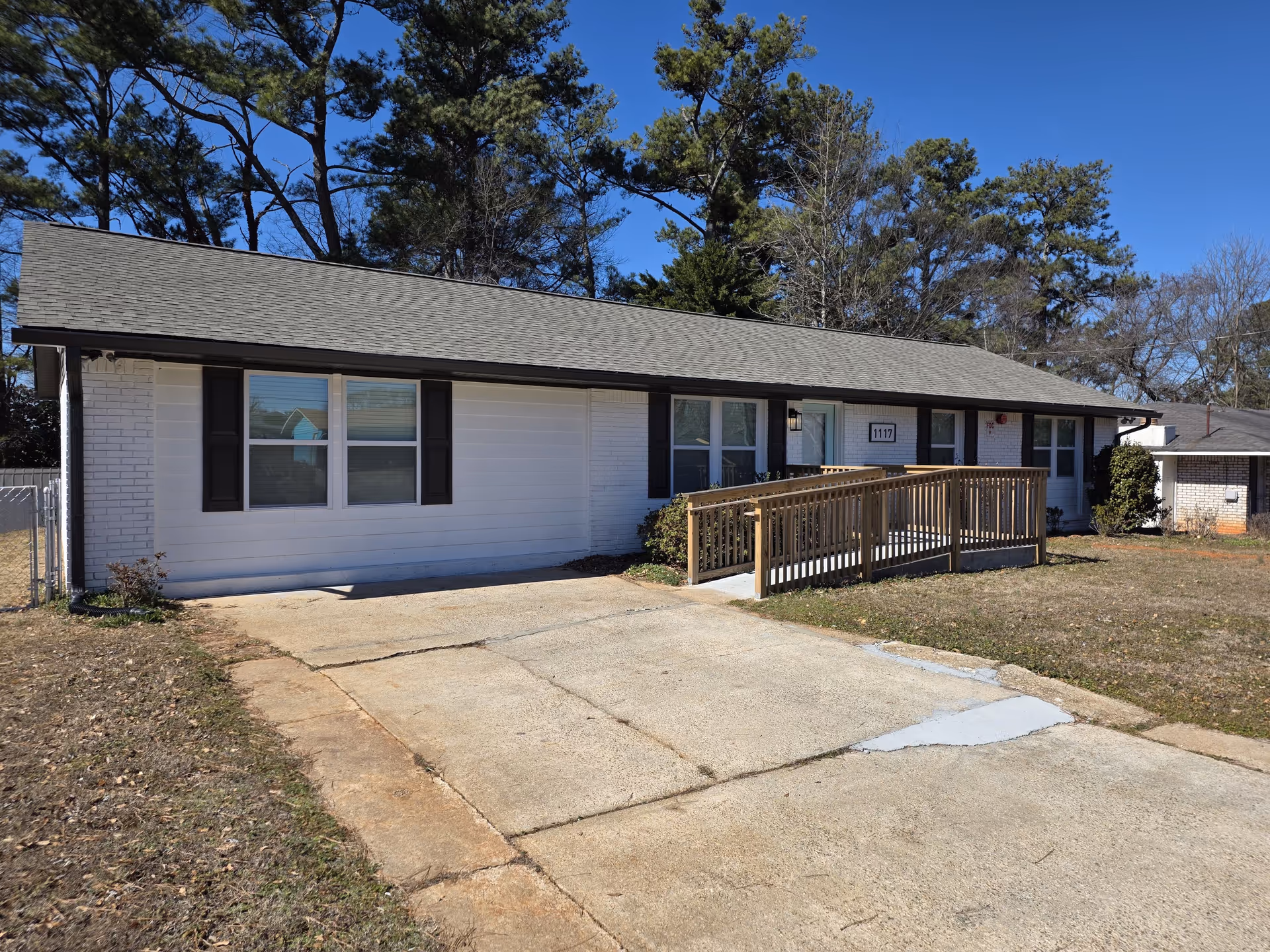 White, single-story care home exterior with ramp, windows, and surrounding trees.