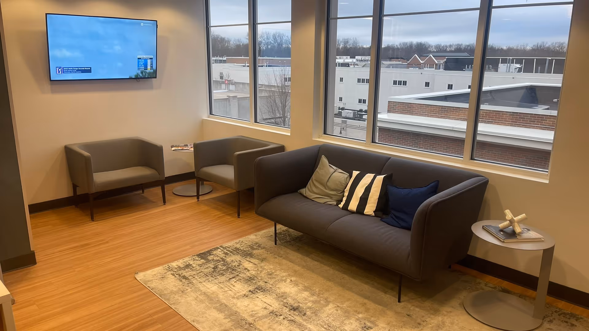 Modern lounge area with sofa, two chairs, coffee table, TV, and large windows.