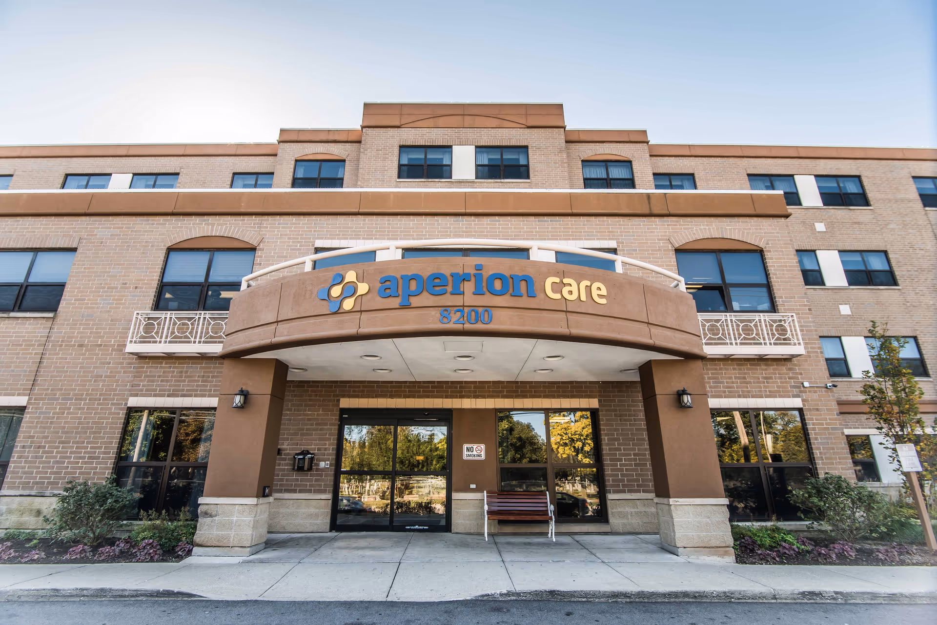 Exterior entrance of a brick senior living building with a curved canopy and Aperion Care sign.