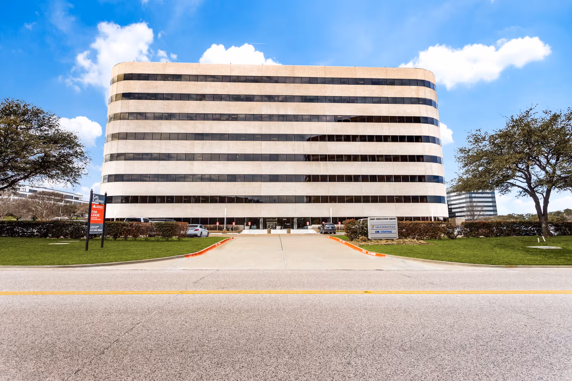 A modern curved, multi-story office building seen from the street with a driveway.