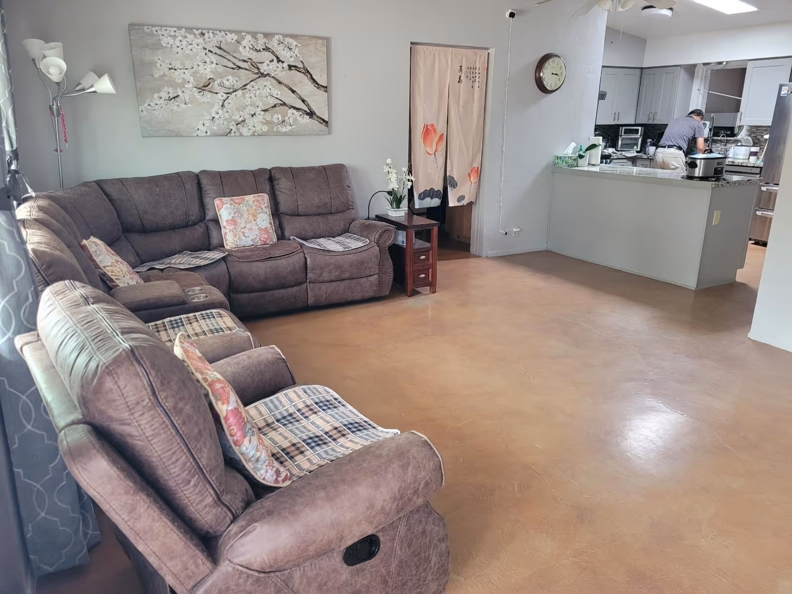 Cozy living room with brown sectional sofas, wall art, and a kitchen in the background.