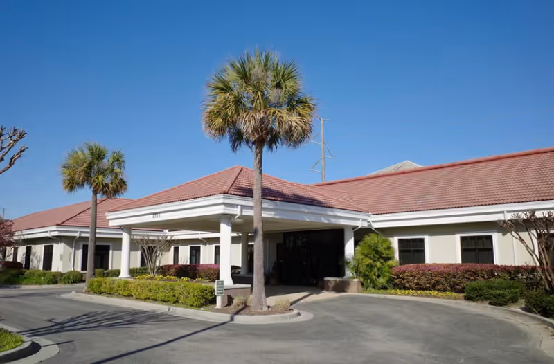 Single-story senior care facility with a covered entrance, palm trees, and manicured landscaping.