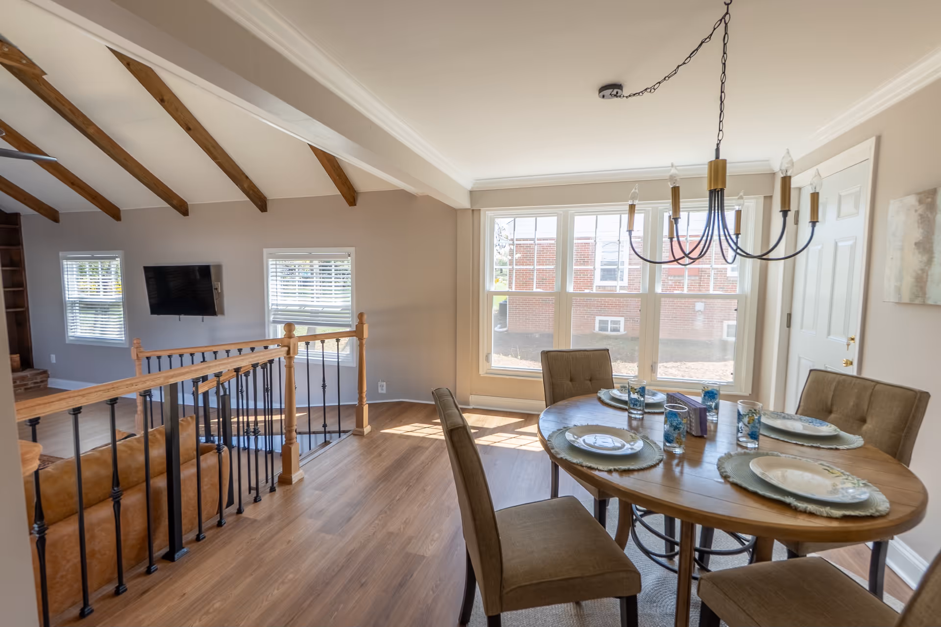 Bright open dining area featuring a wooden table, chairs, chandelier, and large sunlit windows.