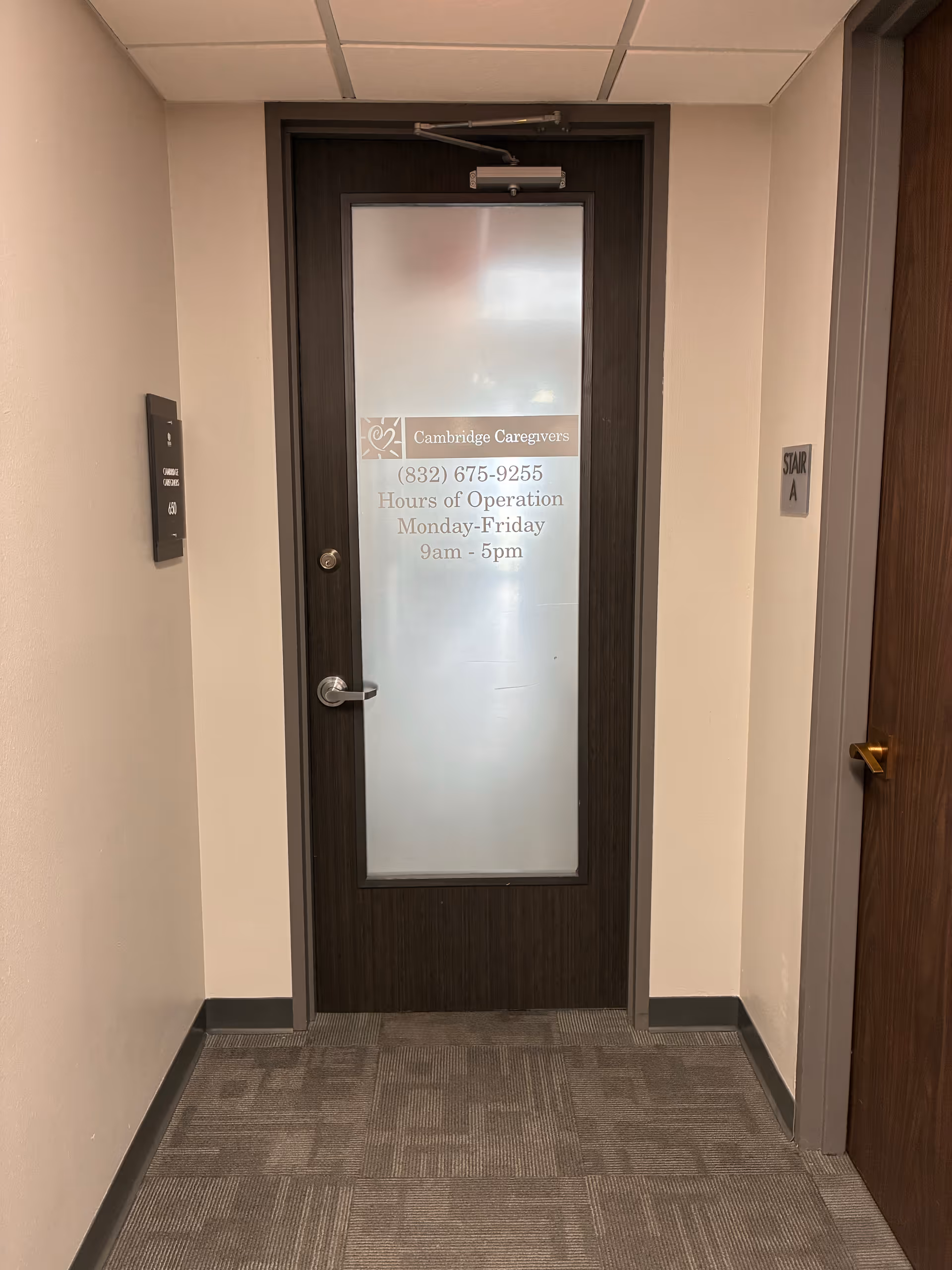 Narrow hallway with a dark wooden door featuring frosted glass and Cambridge Caregivers label.