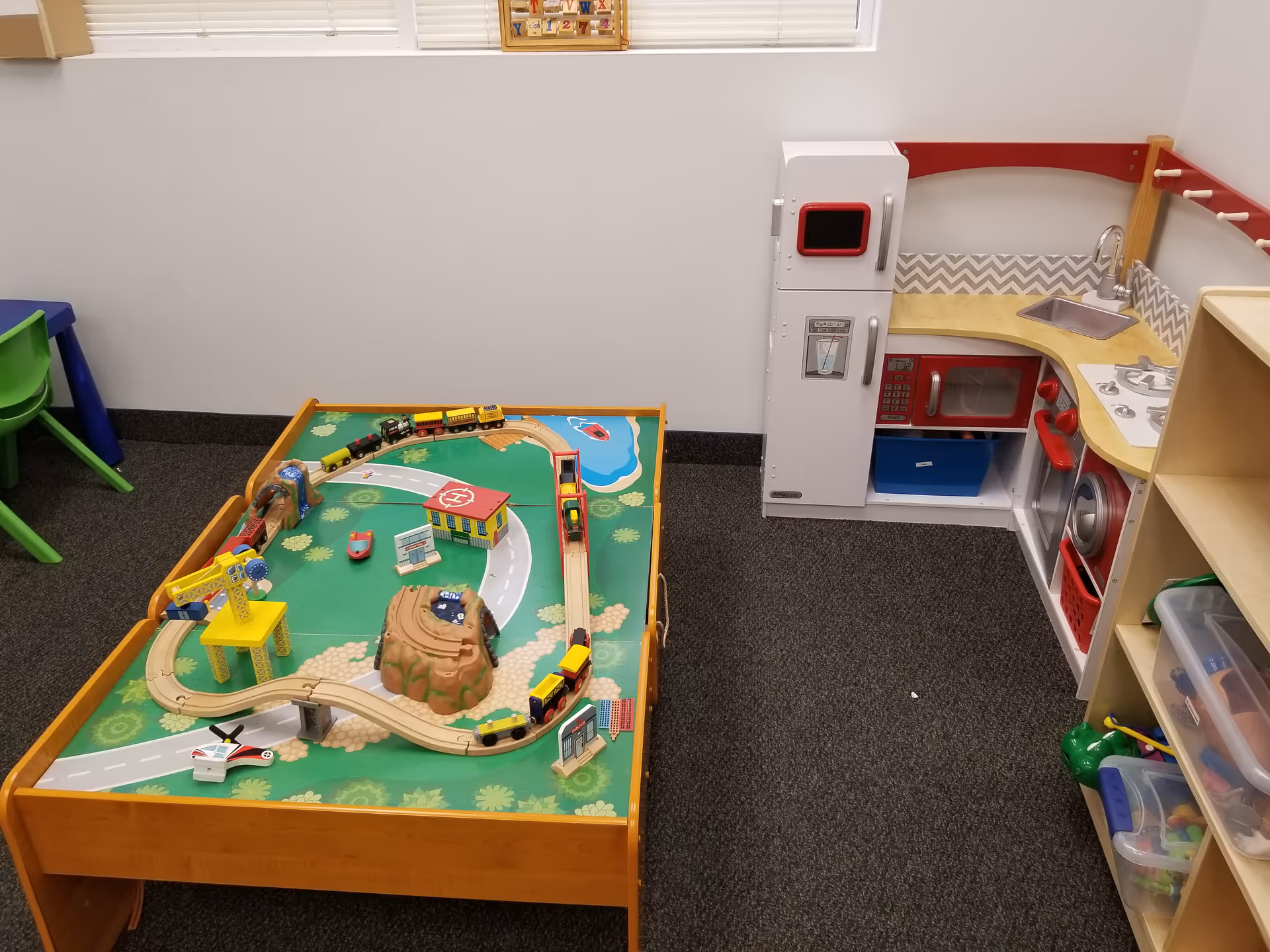 Playroom featuring a toy train layout on a raised table beside a child-sized kitchenette.