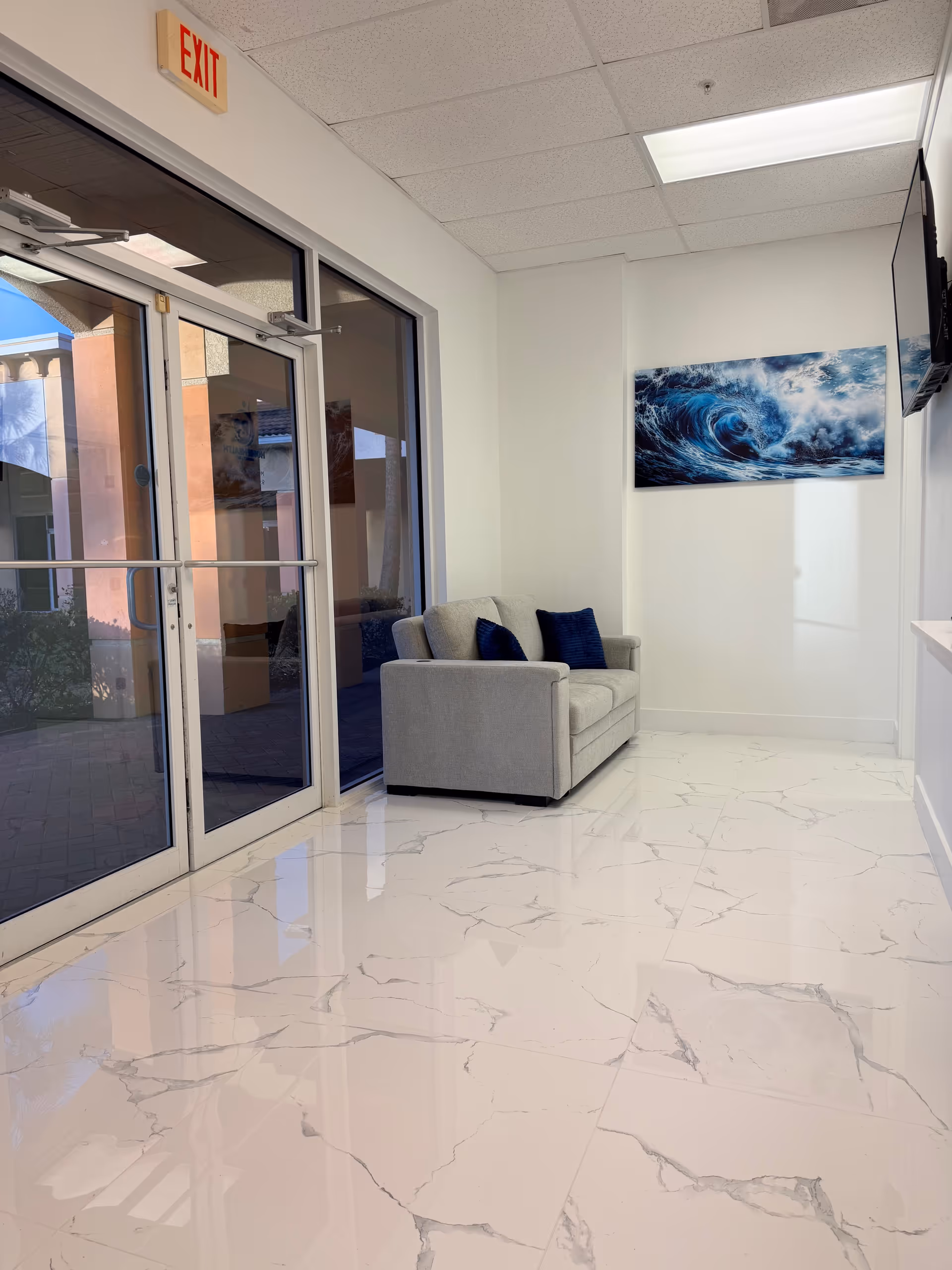 A bright lobby with marble floor, gray sofa, blue cushions, and ocean art.