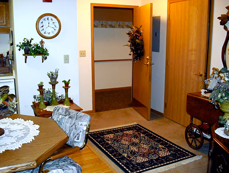 Interior dining area with a wooden table, chairs, rug, and doorway to hallway.