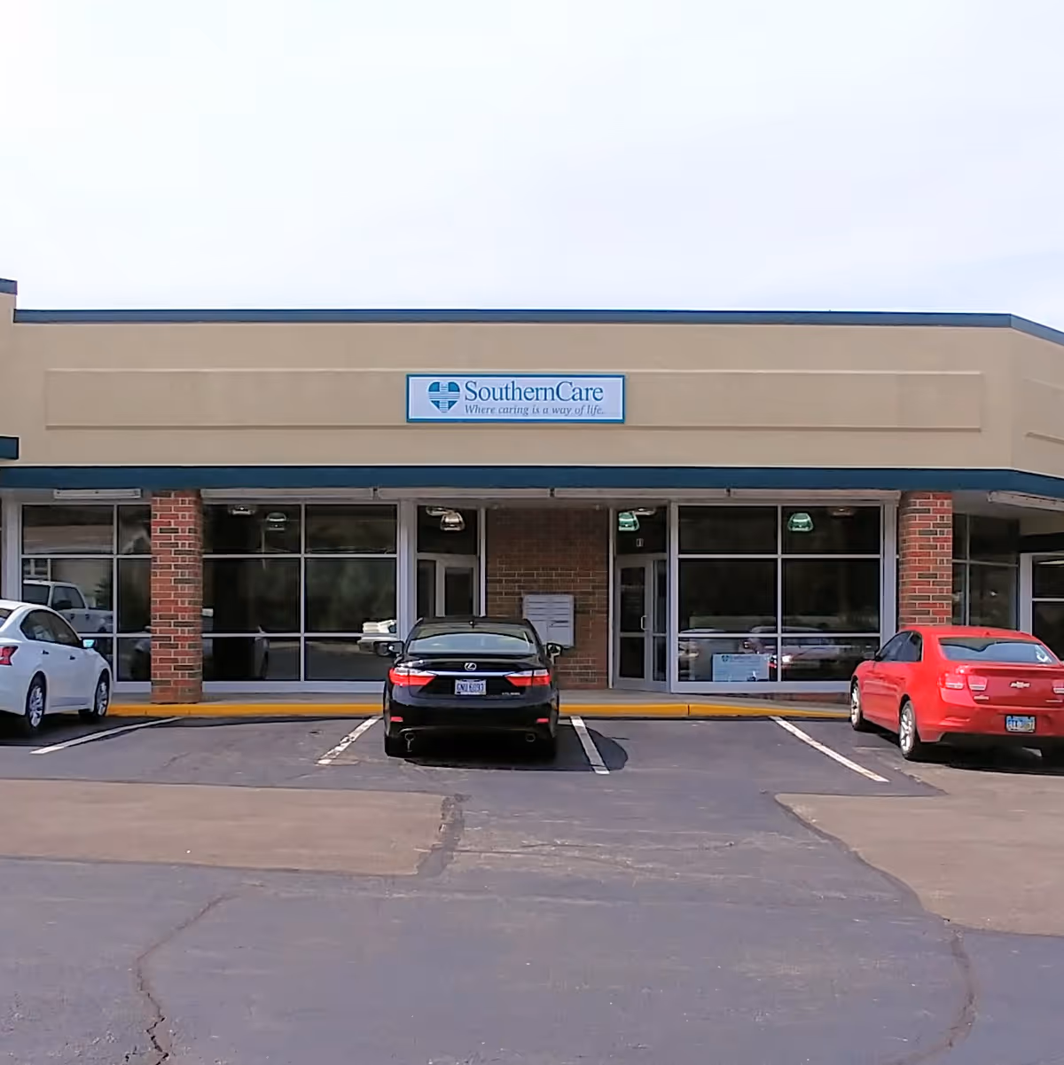 Facade of SouthernCare facility with a sign, brick columns, and parked cars in front.