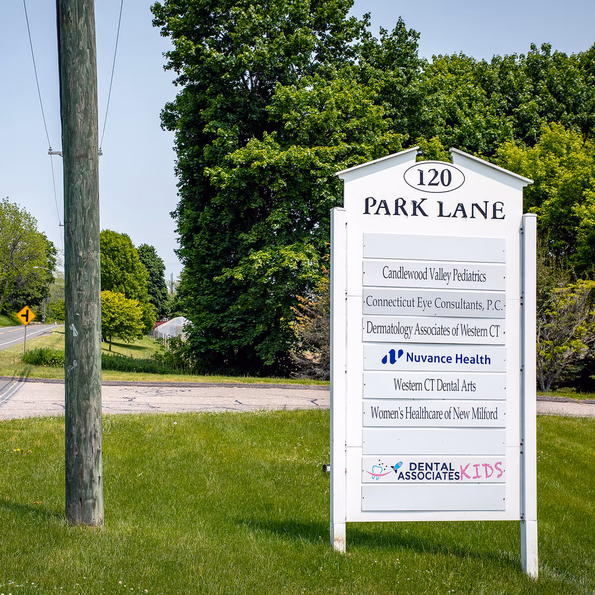 Tall white directory sign with Park Lane address and medical tenants stands beside a road.