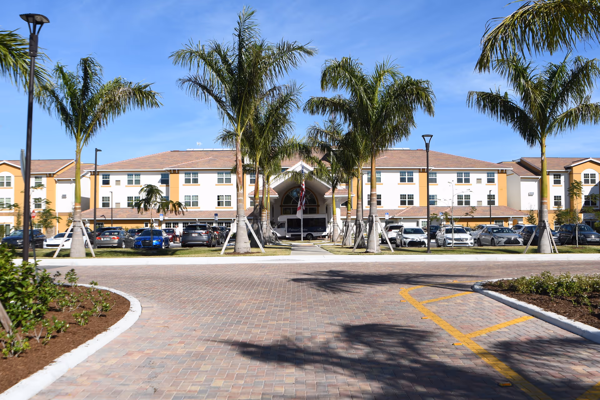 Exterior view of Palomino Gardens Retirement Community with palm trees, parking, and entrance.