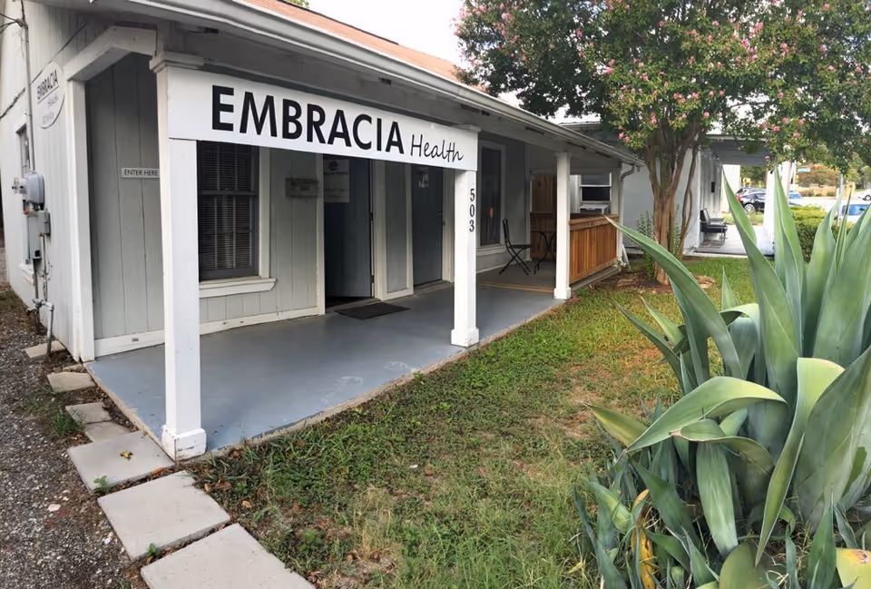 Front view of Embracia Health facility with a covered entrance, porch columns, and surrounding landscaping.