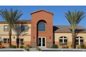 A senior living facility exterior with two palm trees and a central entrance.