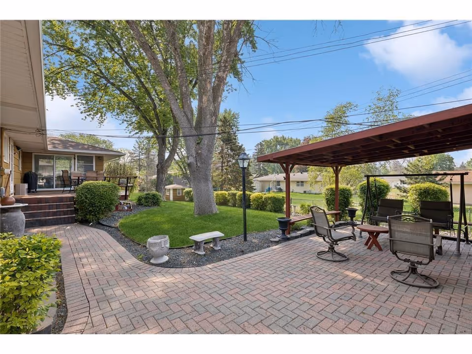 Sunny outdoor patio with seating, lawn, trees, and a covered seating area.