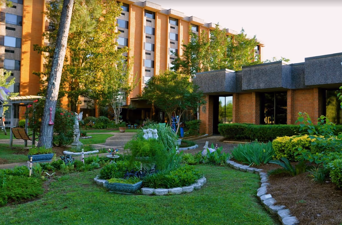 Landscaped courtyard and garden in front of a multi-story brick senior living facility building.