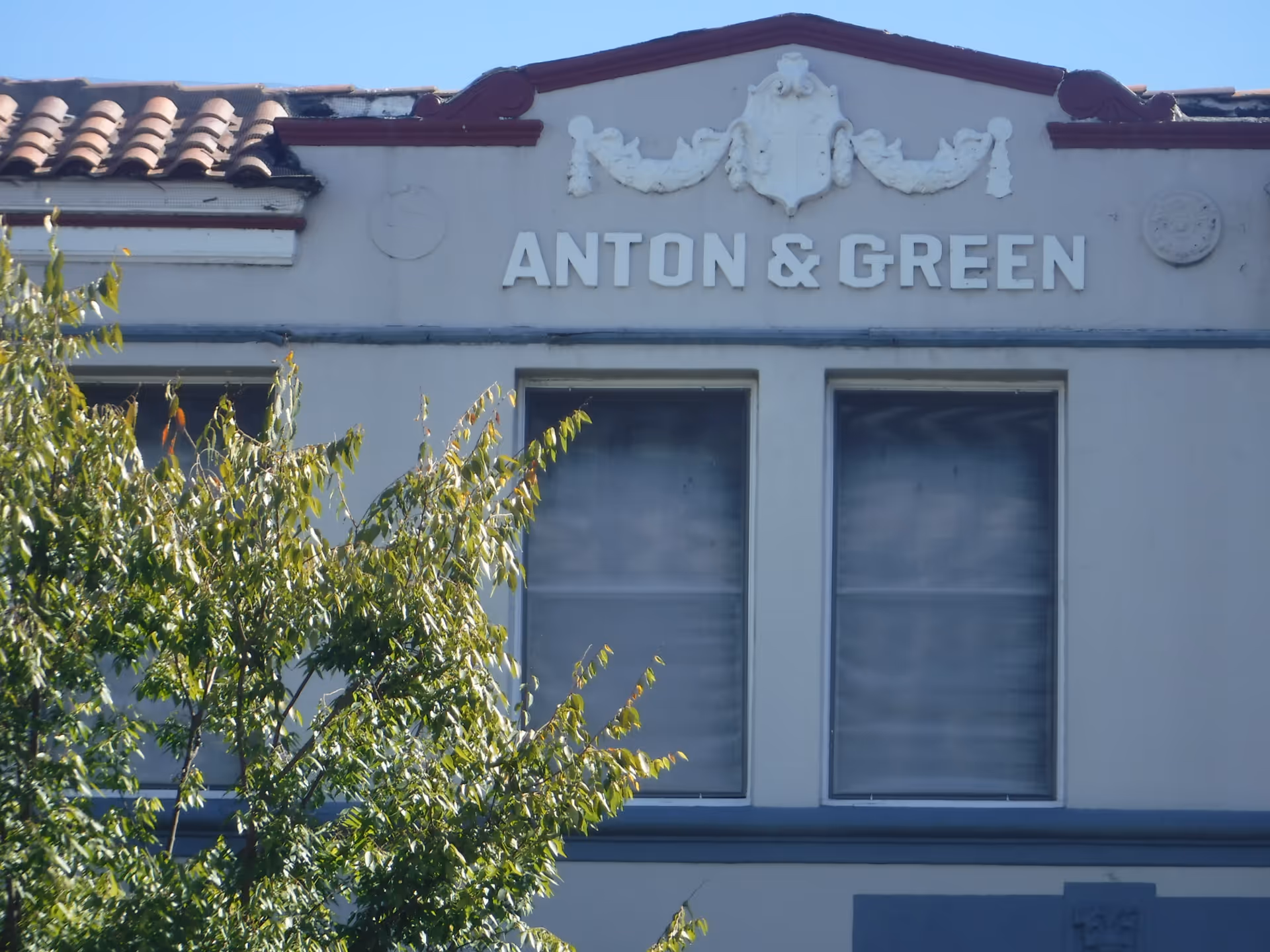 Exterior of a building with Anton & Green sign and trees partly obscuring windows.