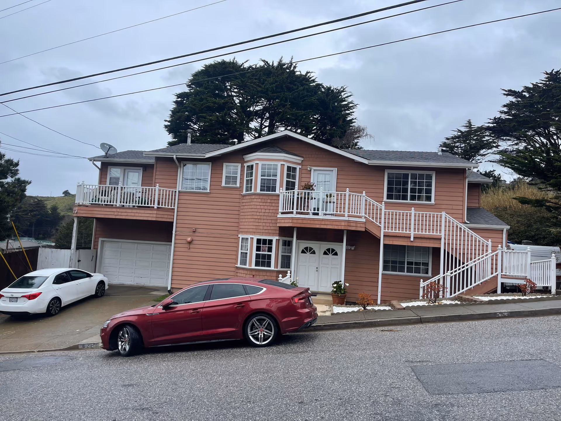 Two-story pink building with white railings, stairs, and parked cars along a street.