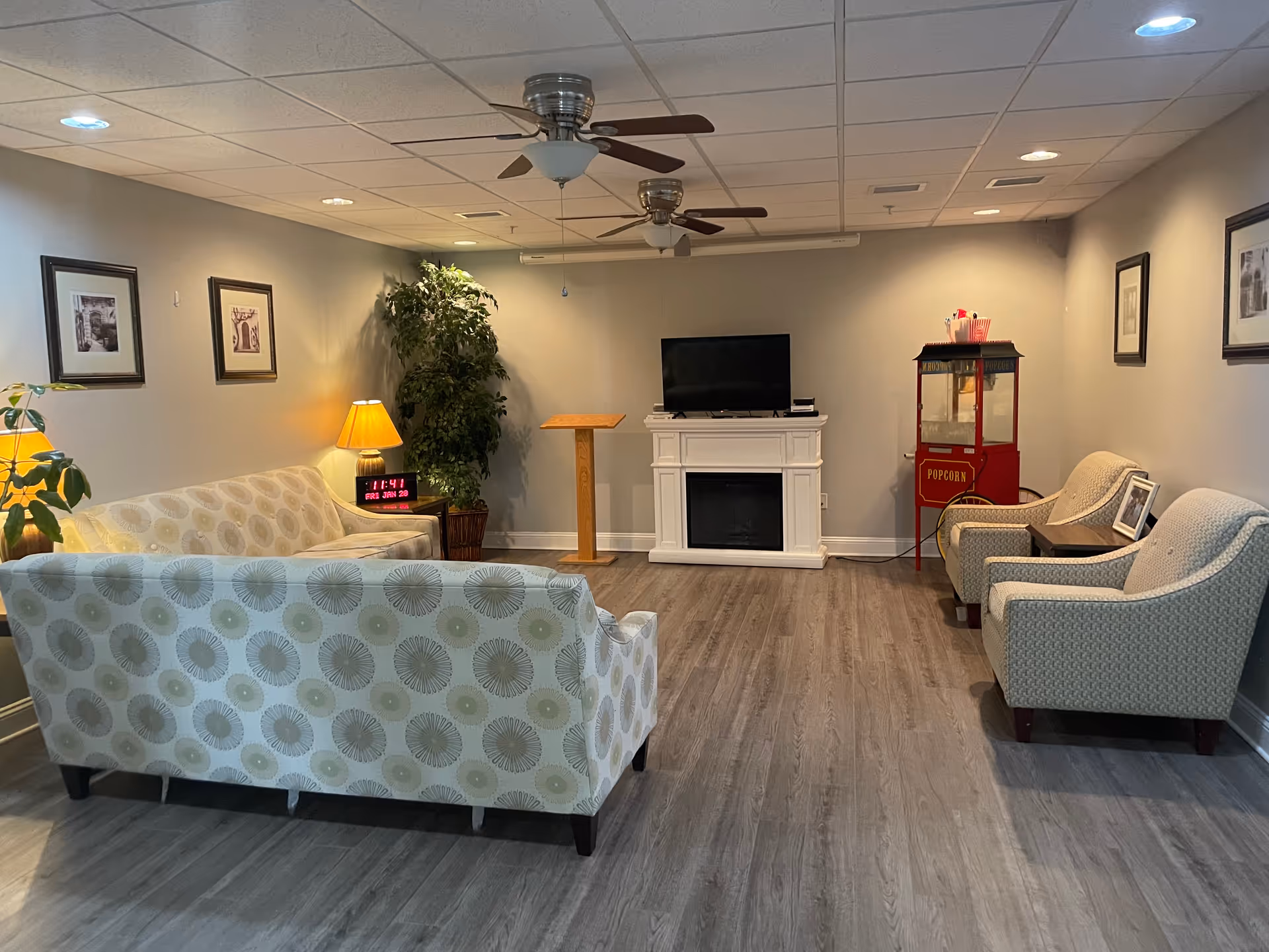 Bright senior living lounge with sofas, chairs, fireplace, TV, and popcorn machine.