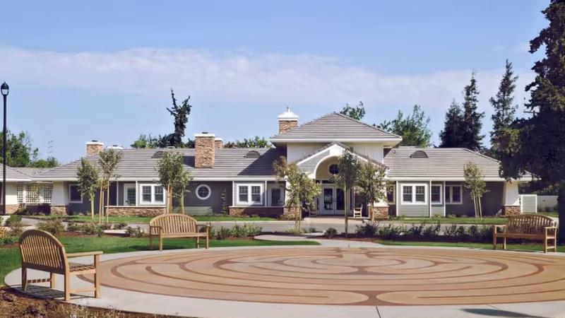Front exterior view of a hospice building with circular plaza and benches.