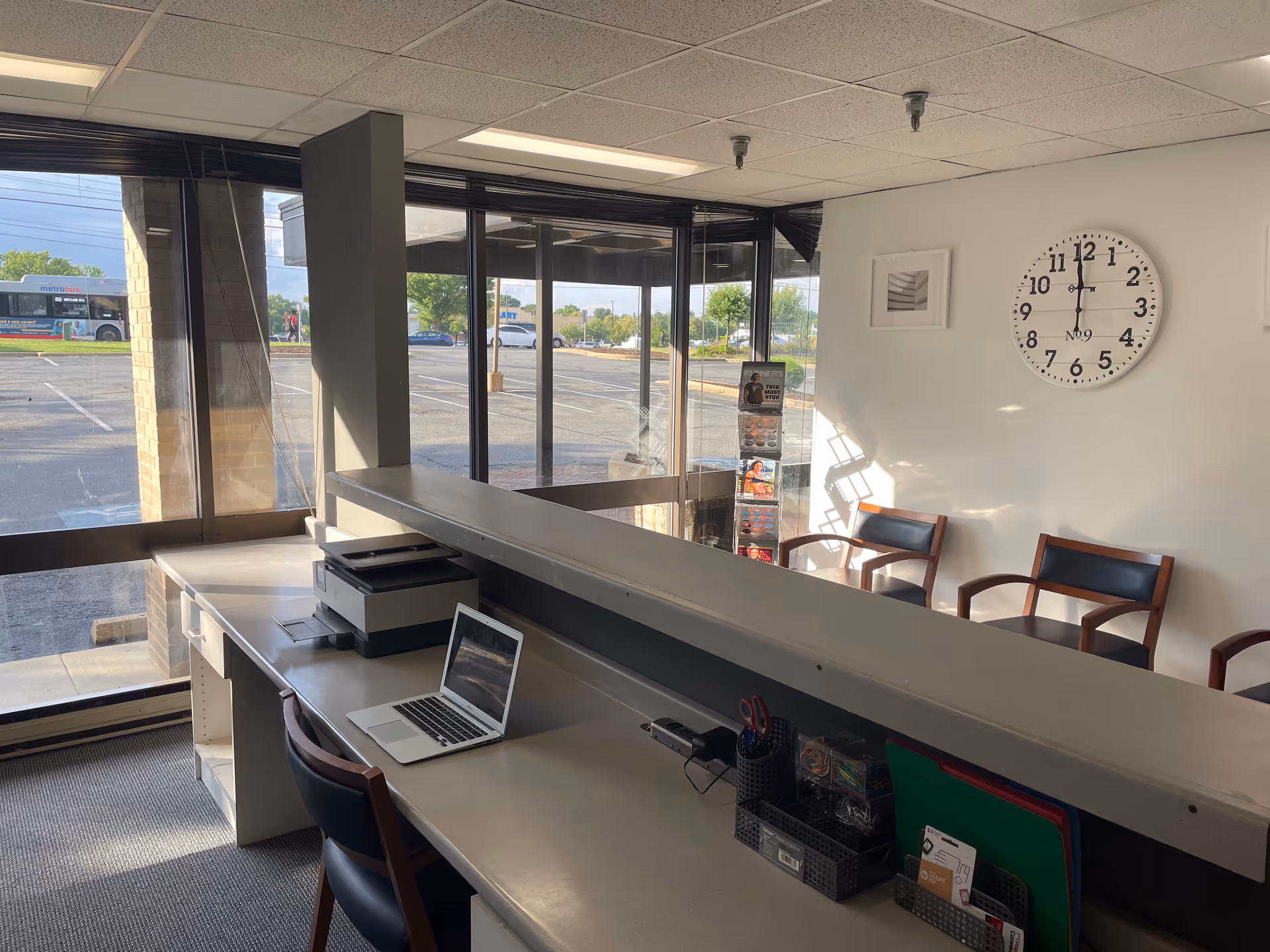 Interior reception area with a long counter, laptop, magazine rack, and wall clock.