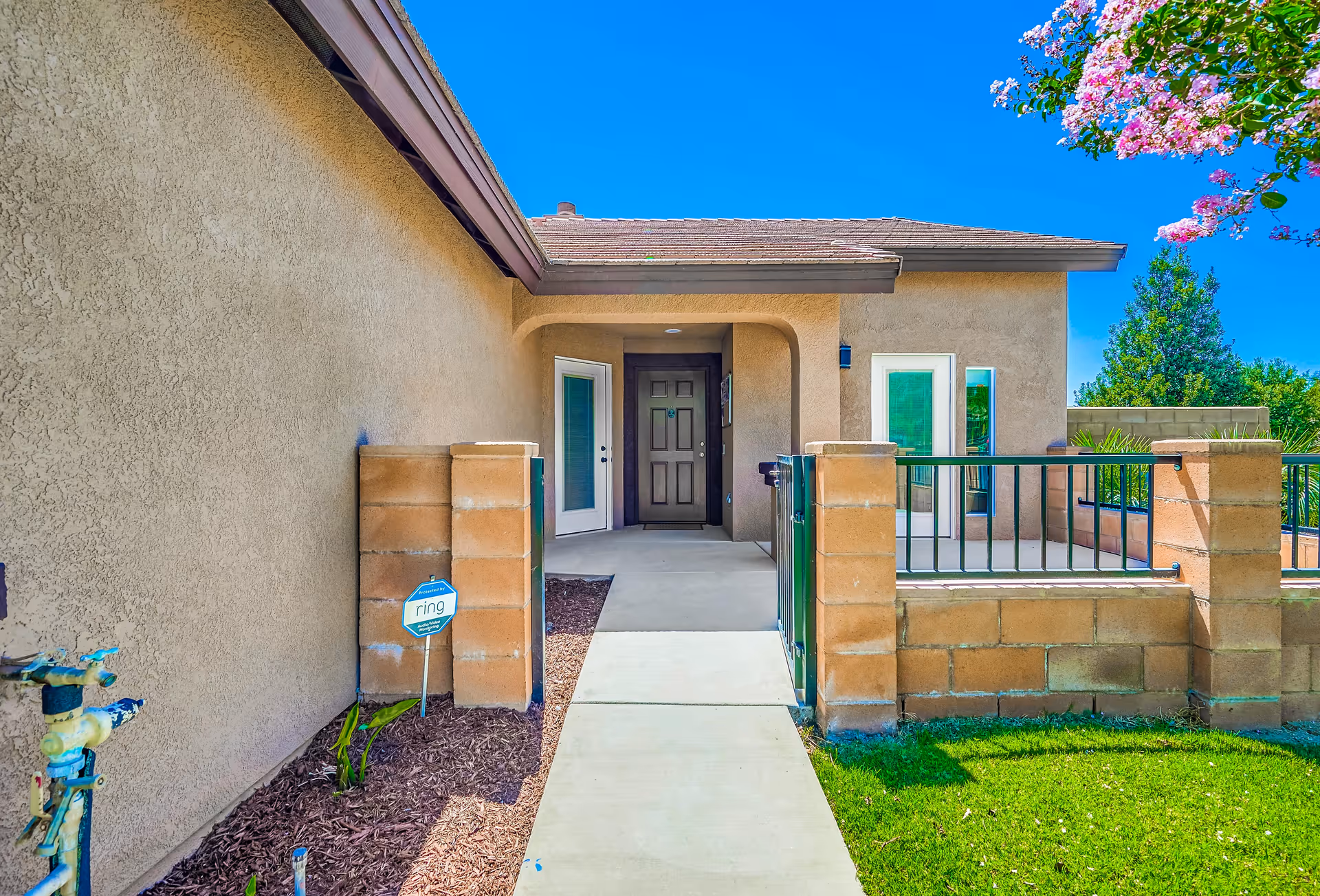 Front entrance of a single-story stucco home with a gated walkway, brown front door, and small porch area.