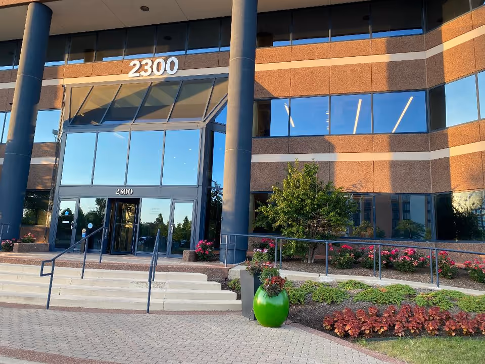 Modern brick building entrance with glass doors, prominent columns, steps, and the number 2300.