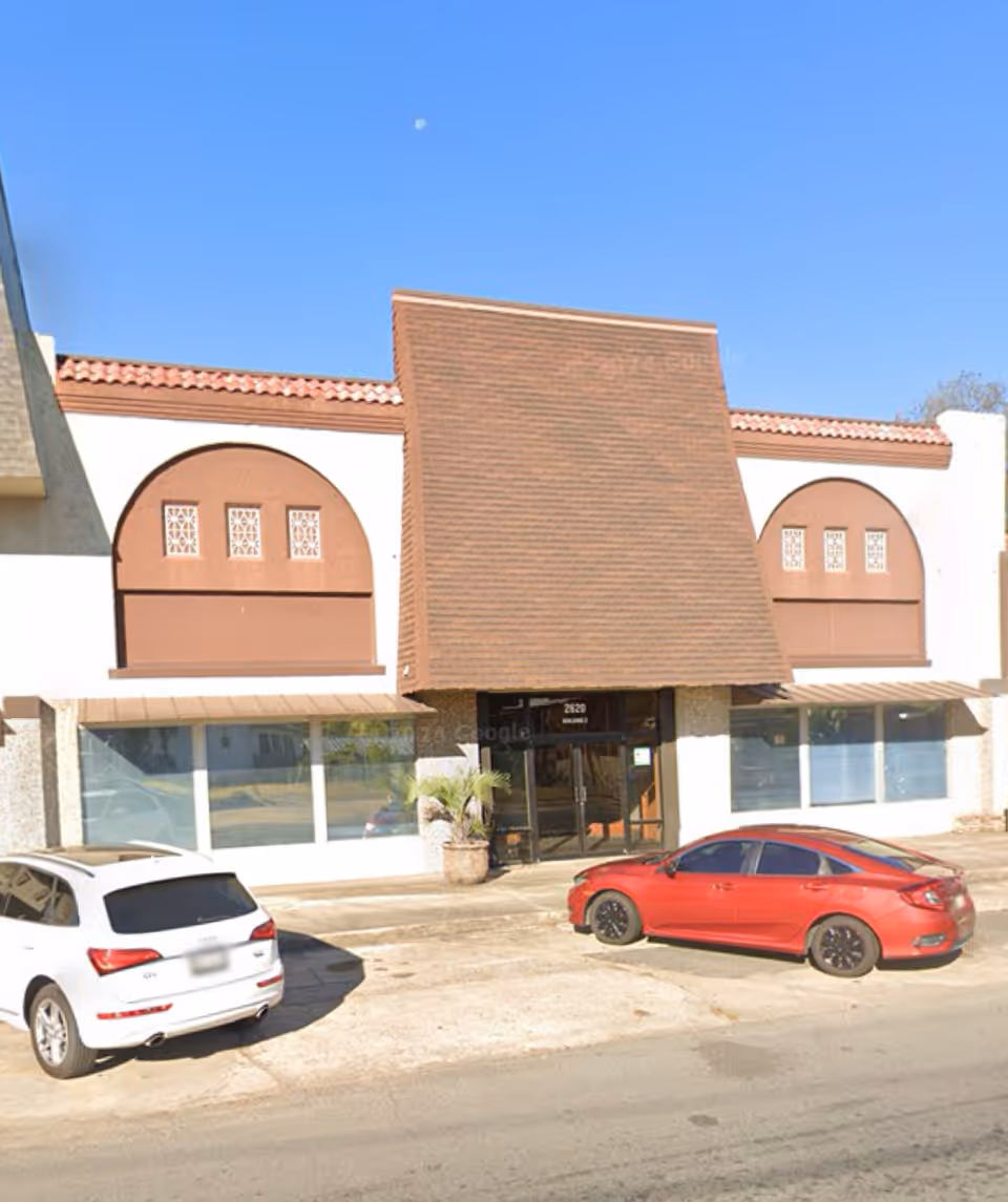 Exterior view of a senior care facility with a slanted brown facade and parked cars.