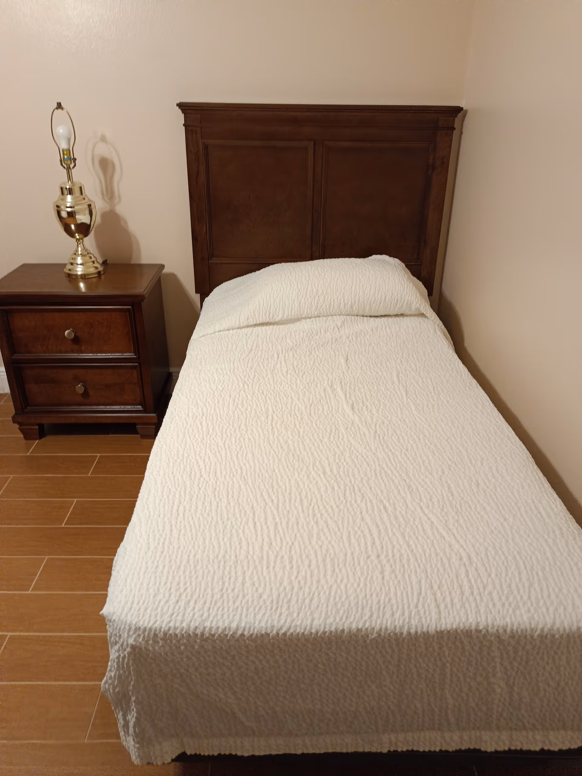 Single bed in a plain bedroom with a wooden headboard and nightstand.