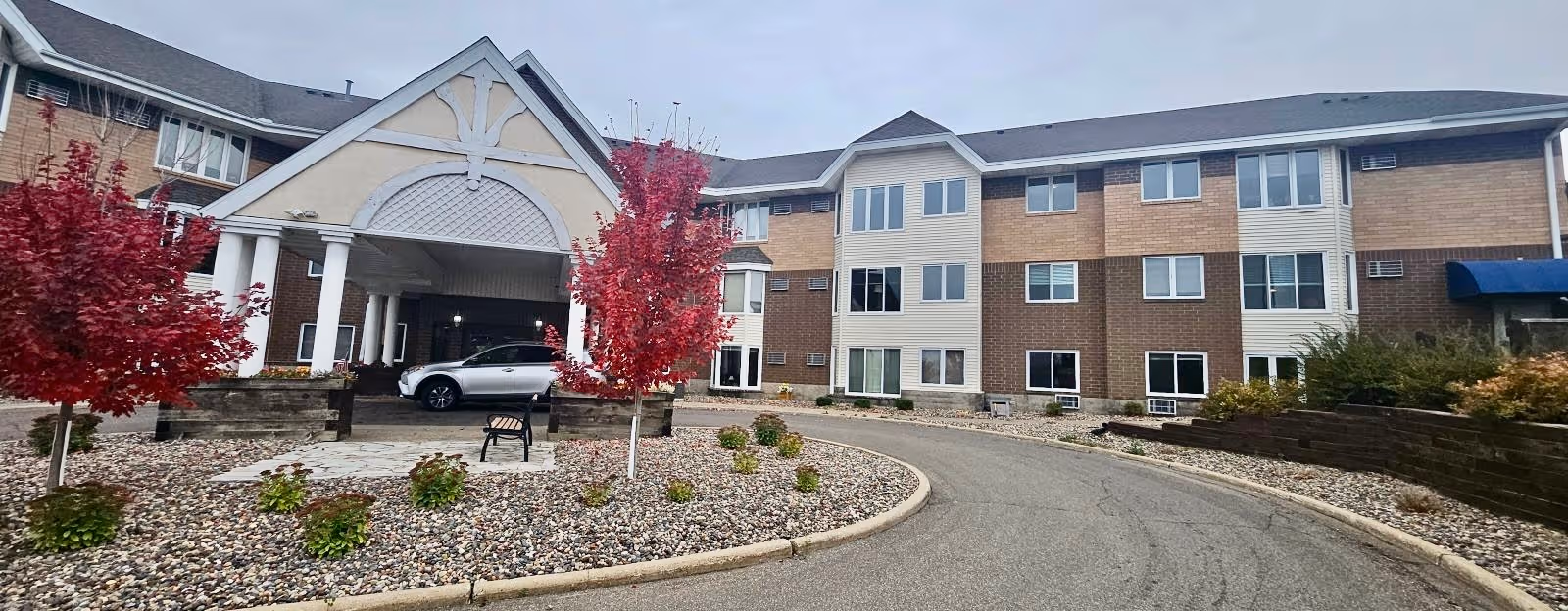 Exterior view of Benedictine Living Community- Red Wing with red trees and curved driveway.