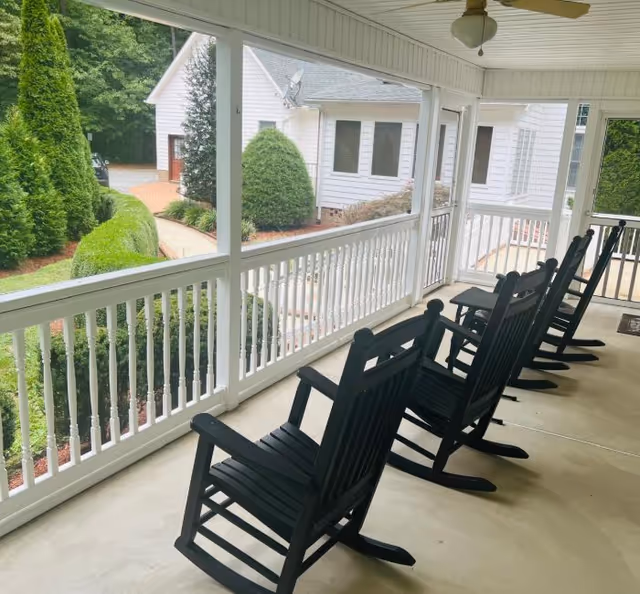 Covered porch with white railings, black rocking chairs, and a neighboring building.