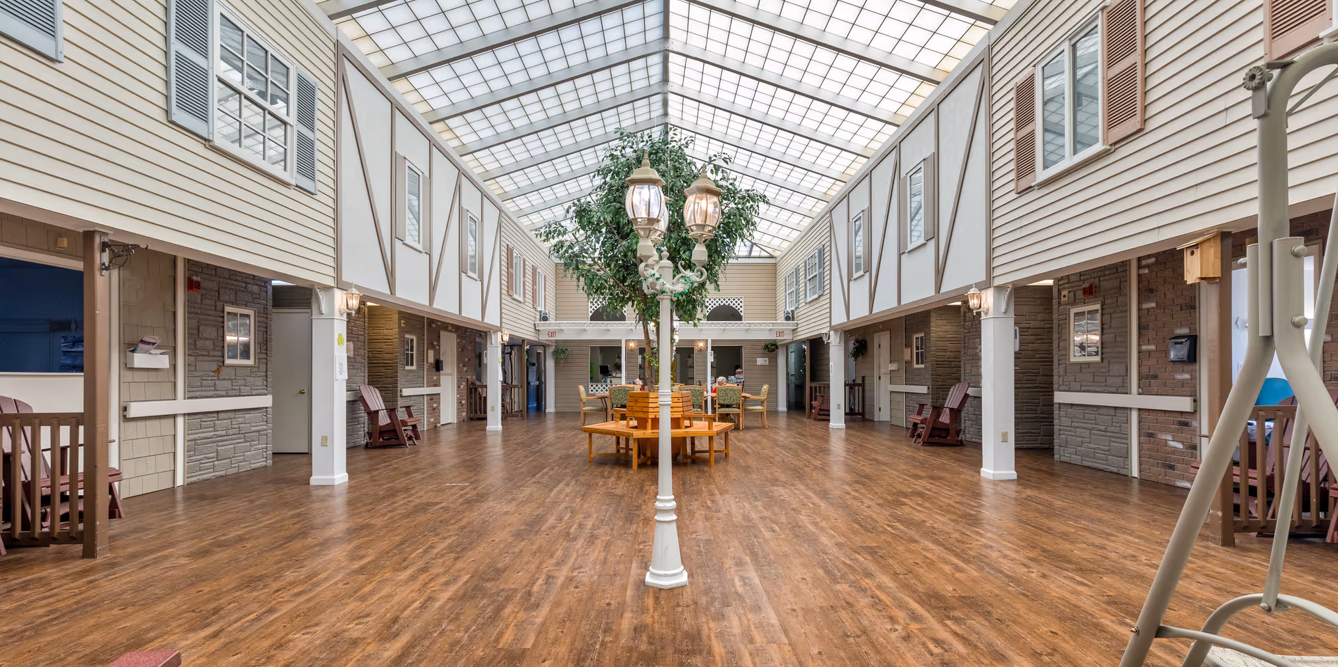 Wide indoor atrium with skylight roof, wood floor, seating tables, and central lamp post.