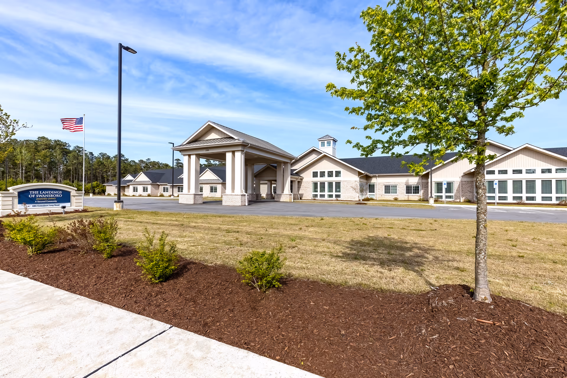 The Landings of Swansboro exterior building with entrance portico, sign, flag, and landscaping.