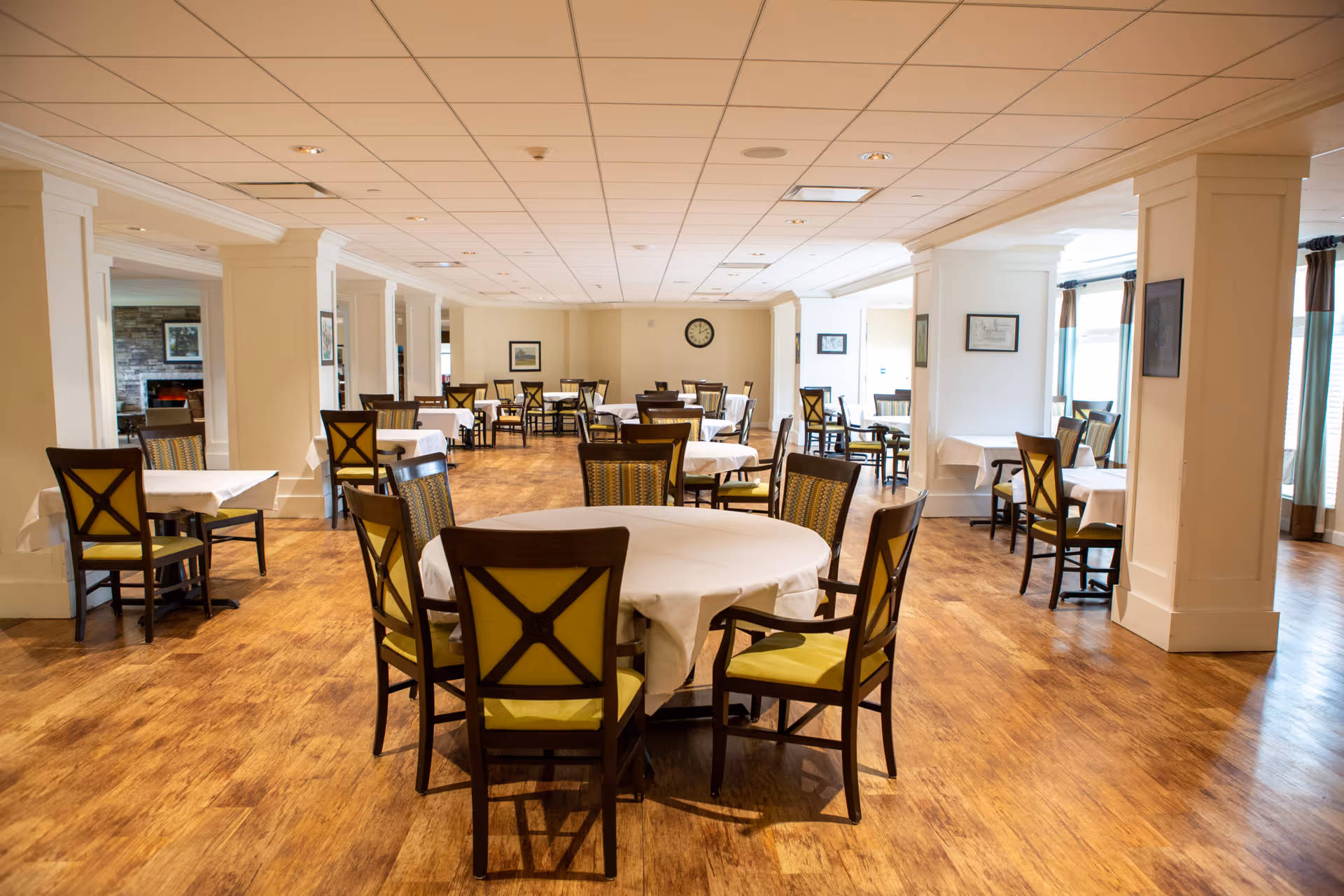 Bright dining hall with round tables, white linens, and wooden chairs in a spacious setting.