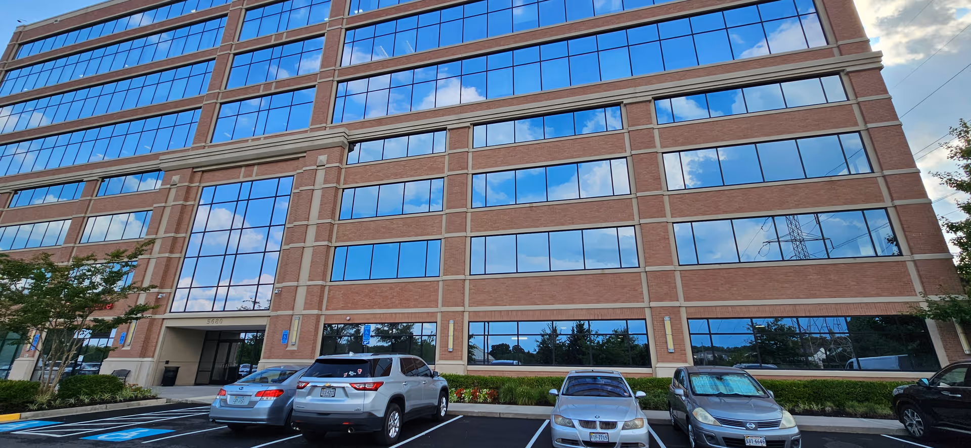 A tall brick building with large blue-tinted windows and a front parking lot.