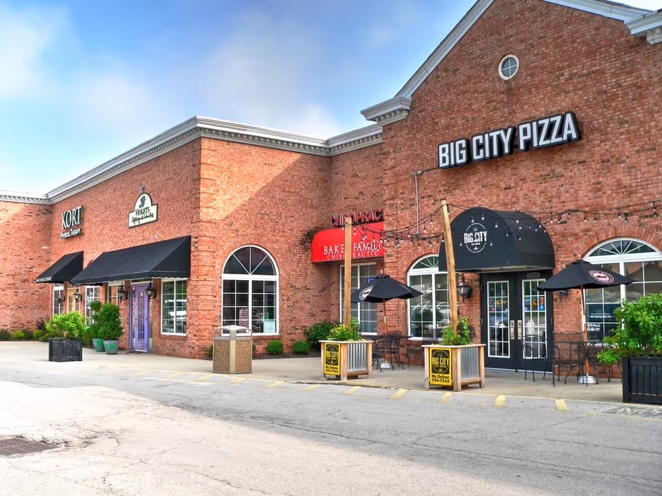 Brick shopping plaza exterior featuring Big City Pizza and outdoor seating.