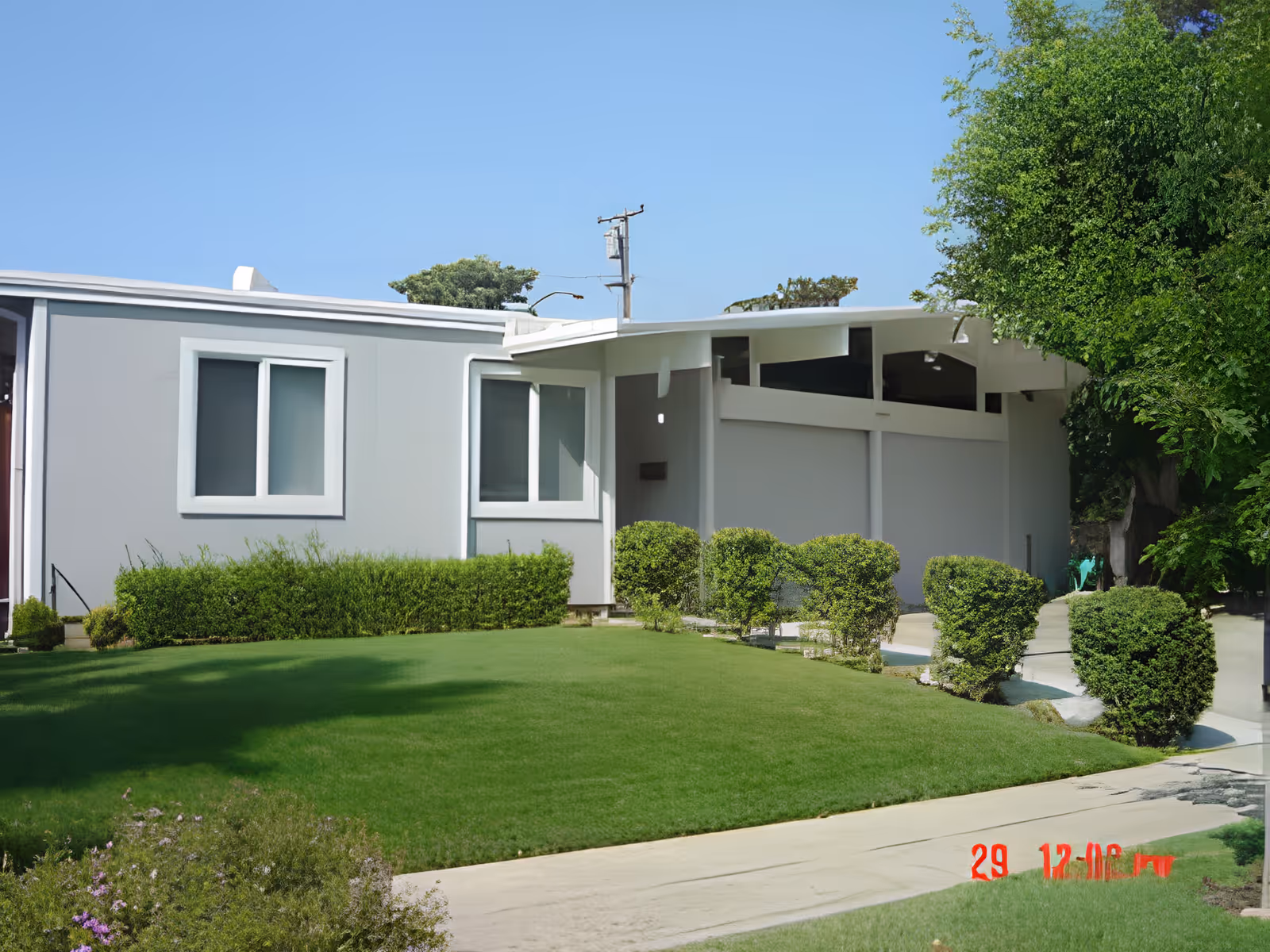 Single-story building front with a manicured lawn, trimmed shrubs, and a driveway under a clear blue sky.