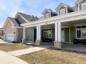 Covered front entrance of a light-green residential building with white columns, dormer windows, and a driveway.