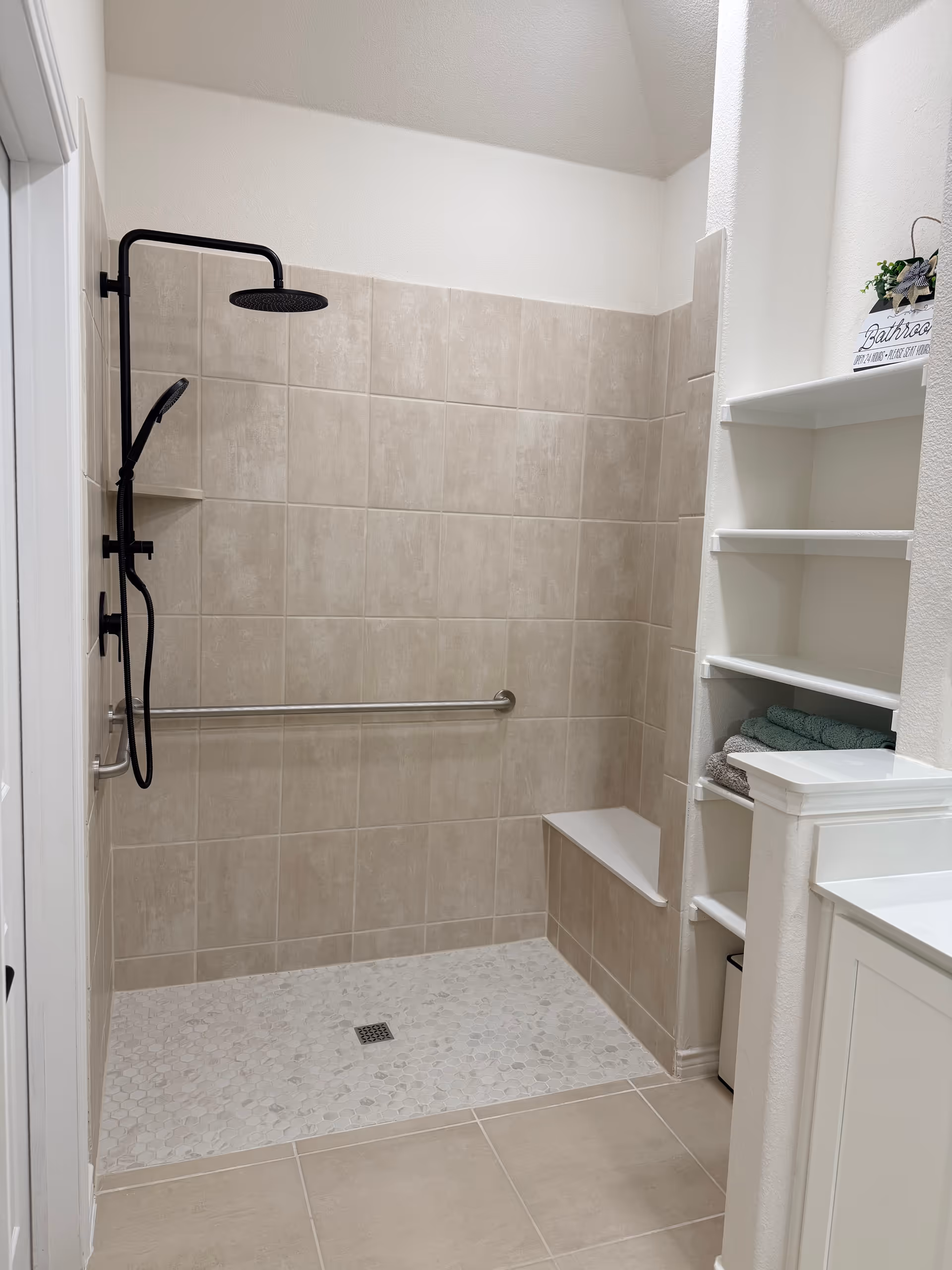 Walk-in tiled bathroom with a shower, grab bar, bench, and open shelves.