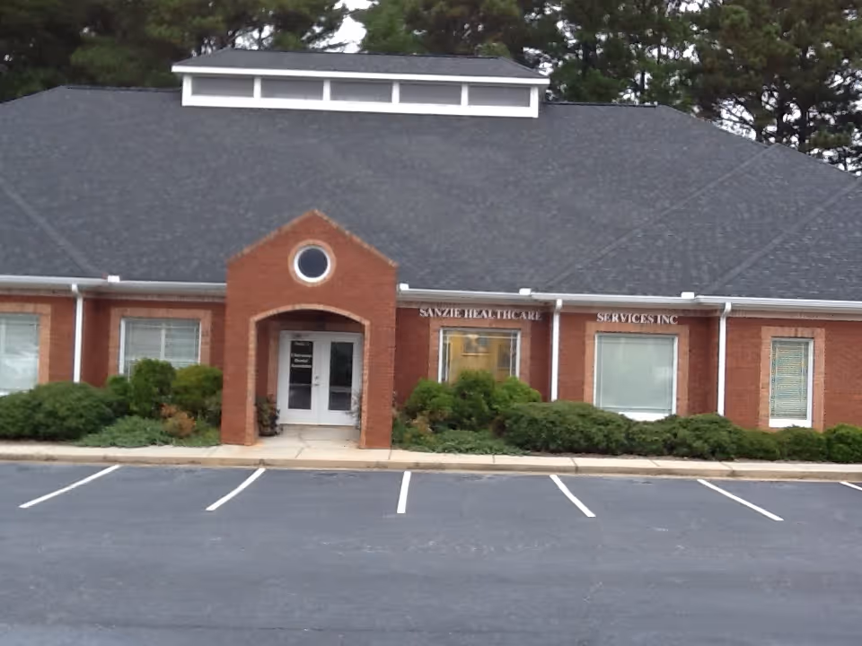 Brick building labeled Sanzie Healthcare Services, Inc., with a curved entry and manicured shrubs.