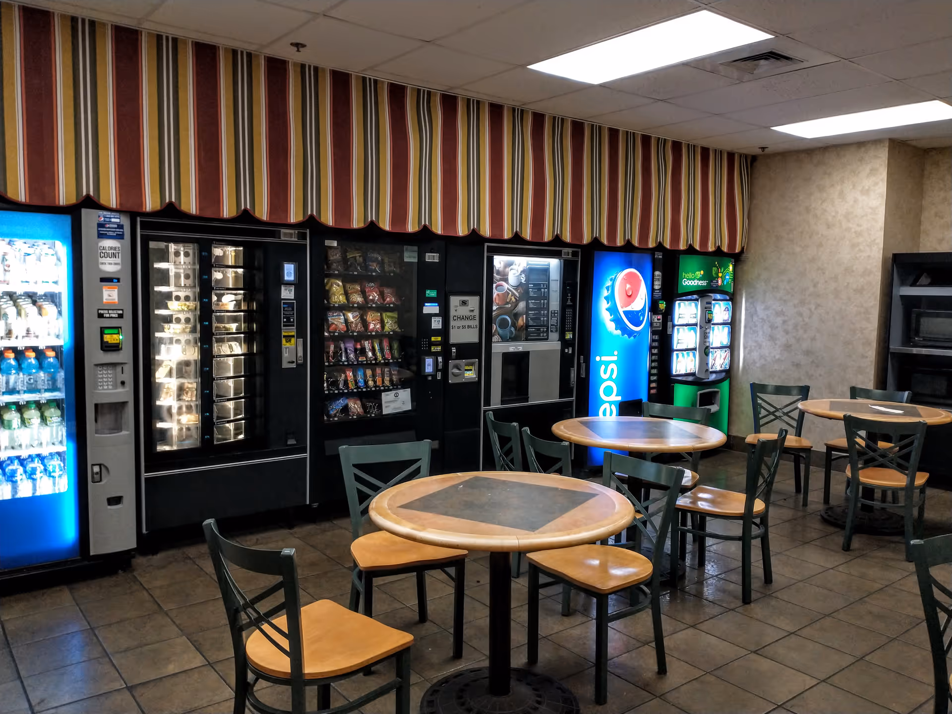 Interior break area with vending machines, snack shelves, and round tables with chairs.