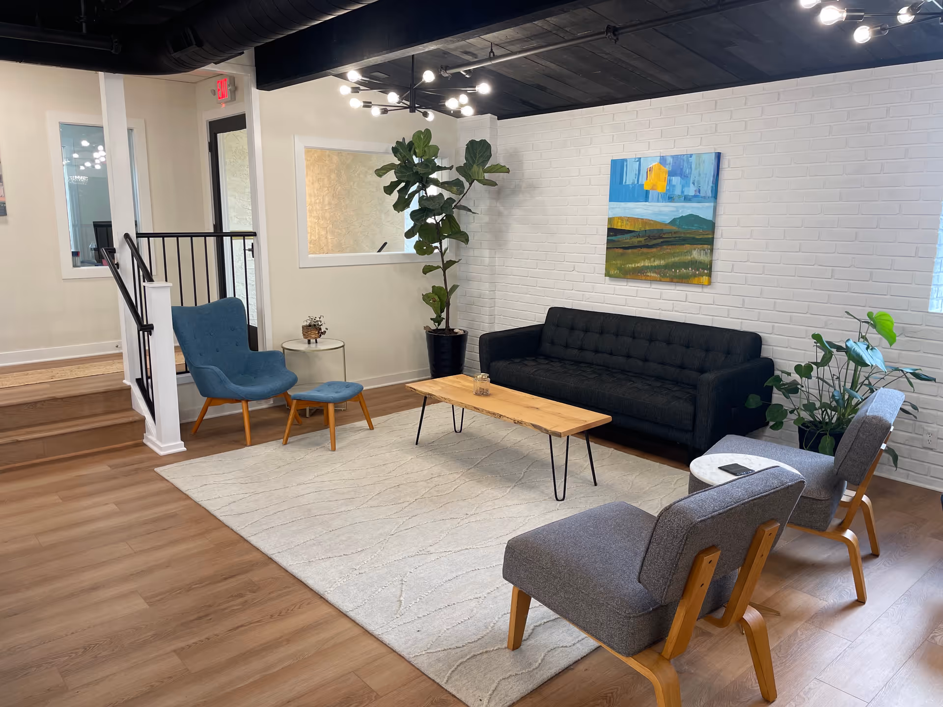 Modern lounge area with sofa, chairs, coffee table, plants, and wall art.
