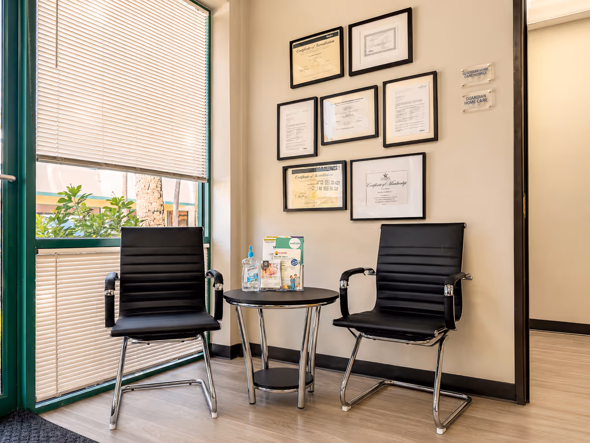 Two black chairs sit beside a round table in a certificate-decorated interior waiting area.