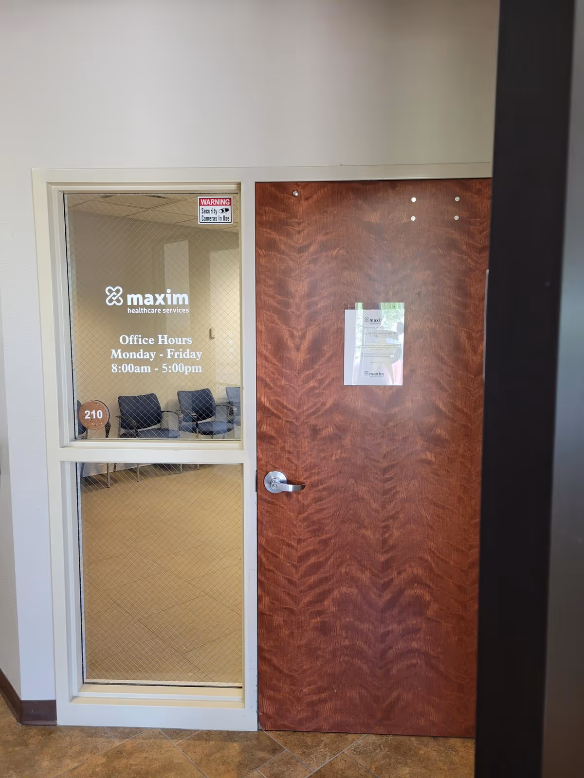 Interior office doorway with Maxim Healthcare Services sign, hours, and seating visible through glass.