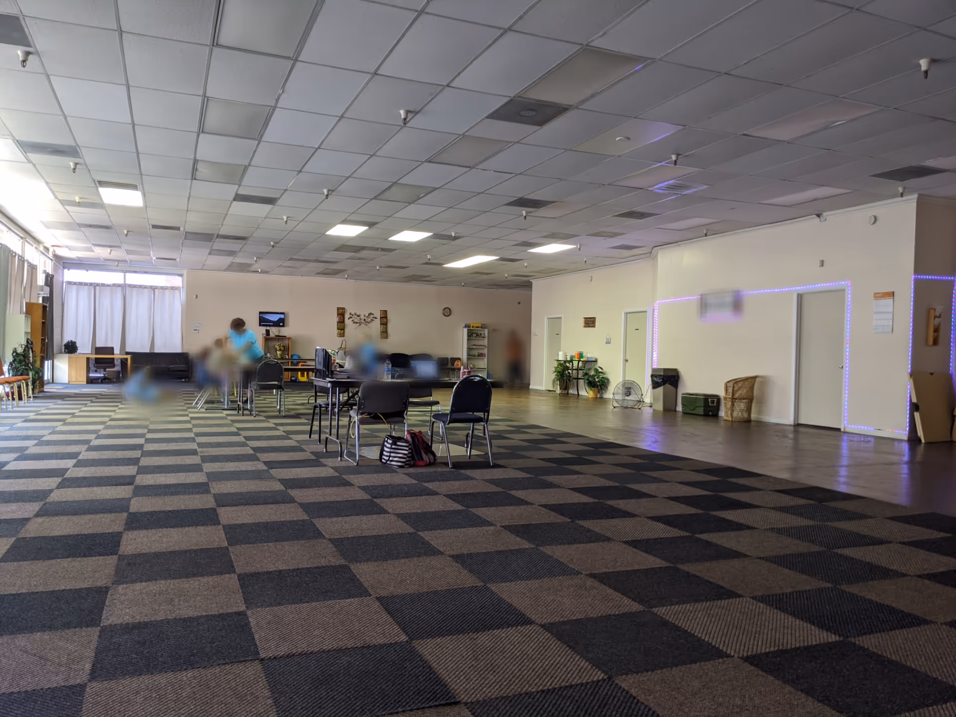 A large open activity room with tables, chairs, blurred residents, and LED-lit wall accents.