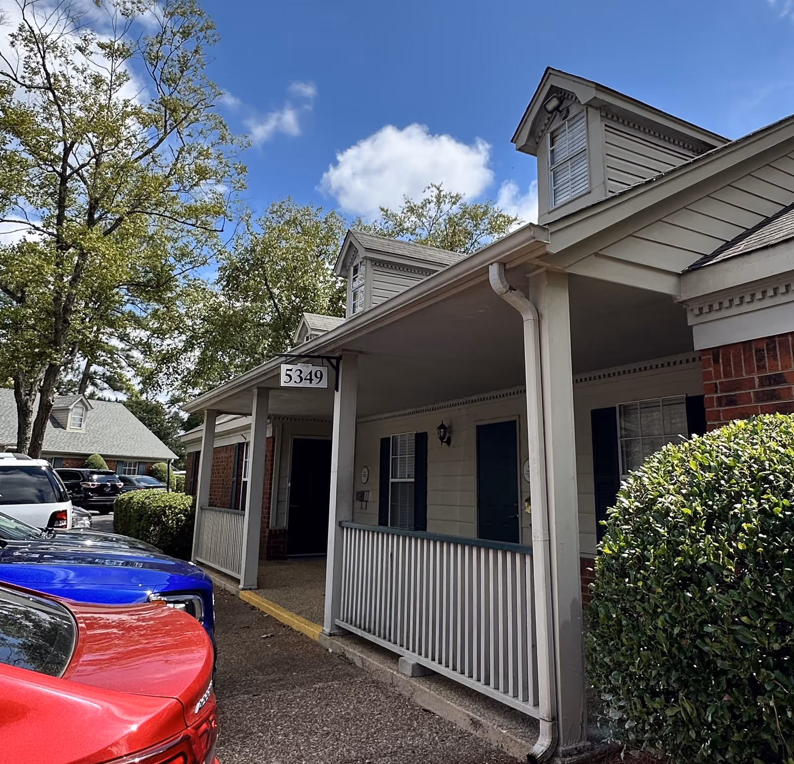 A single-story building exterior with a covered porch and parked cars.