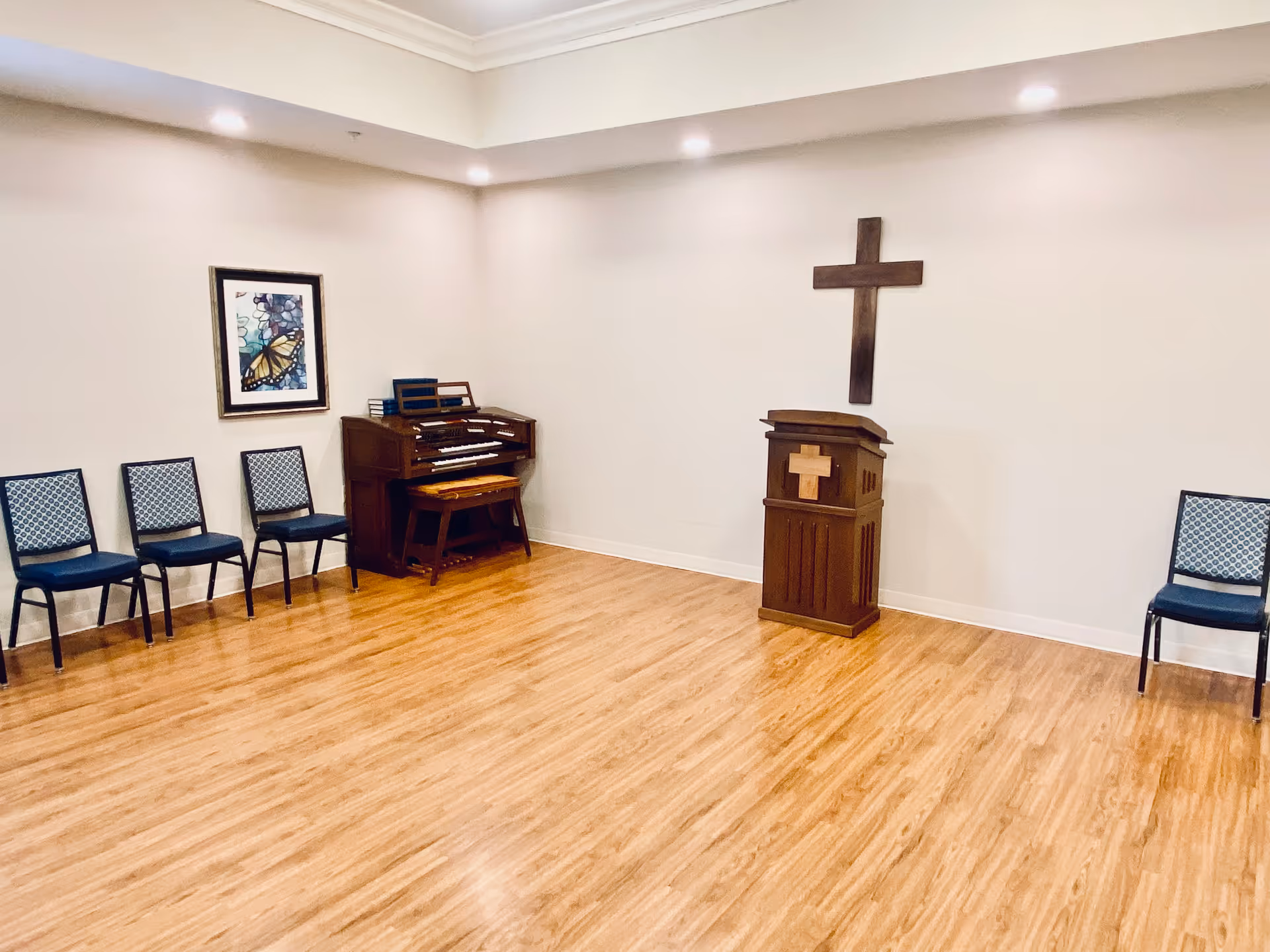 A small interior chapel in a senior facility with a cross, piano, and chairs.