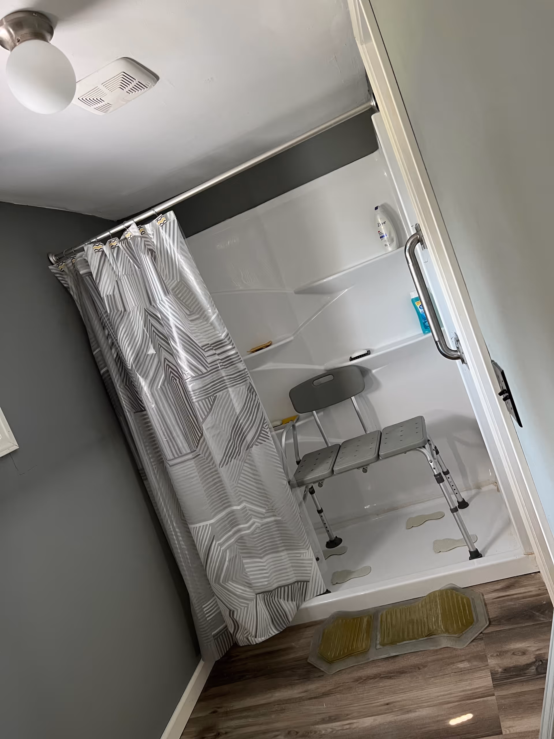 A small accessible shower stall with a curtain, built-in seat, grab bar, and non-slip mats.