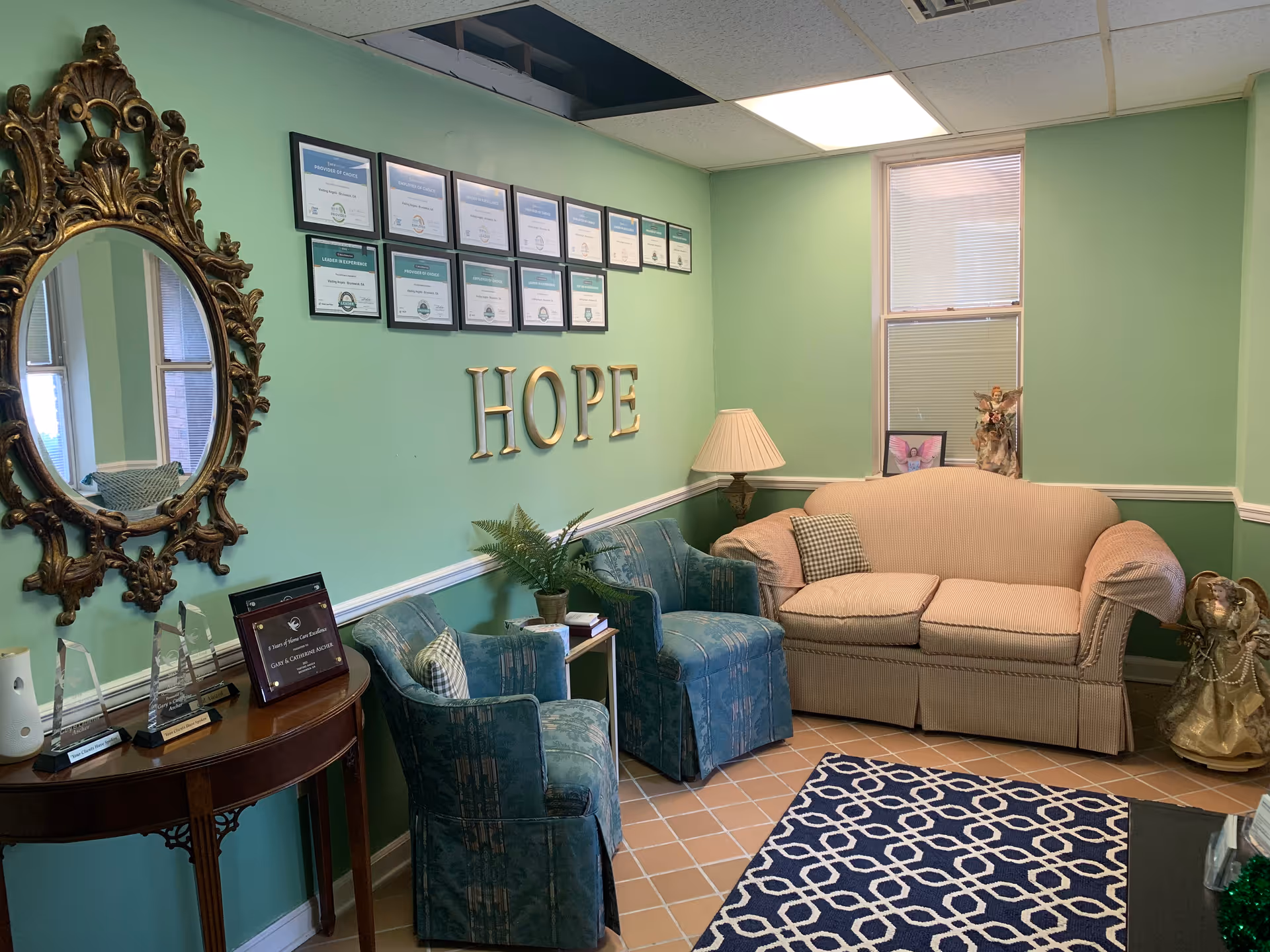 Teal-walled lounge area with beige sofa, teal chairs, certificates, and a HOPE sign.