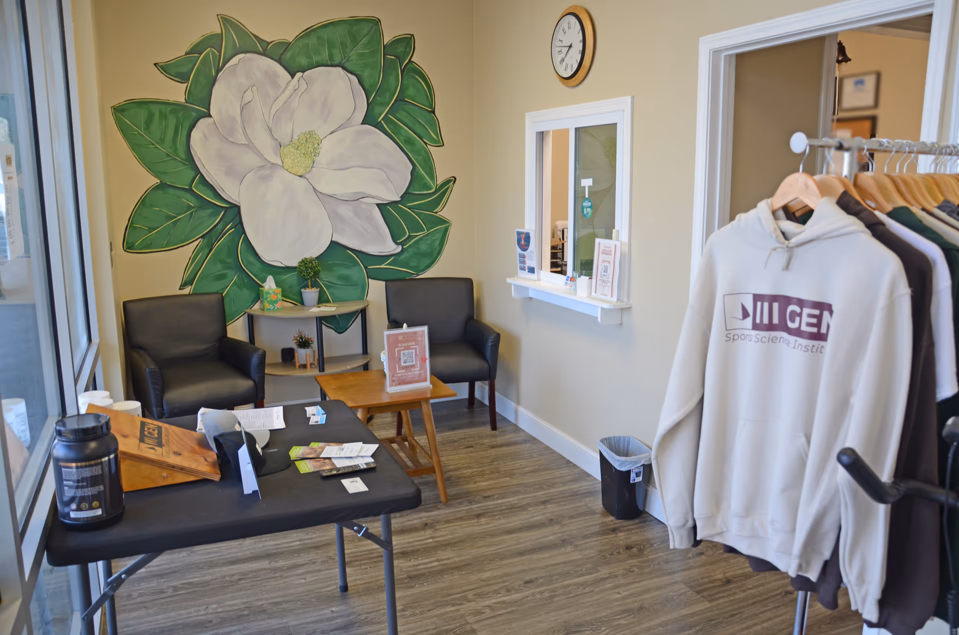 Interior lobby with chairs, a large magnolia mural, window counter, and clothing rack.