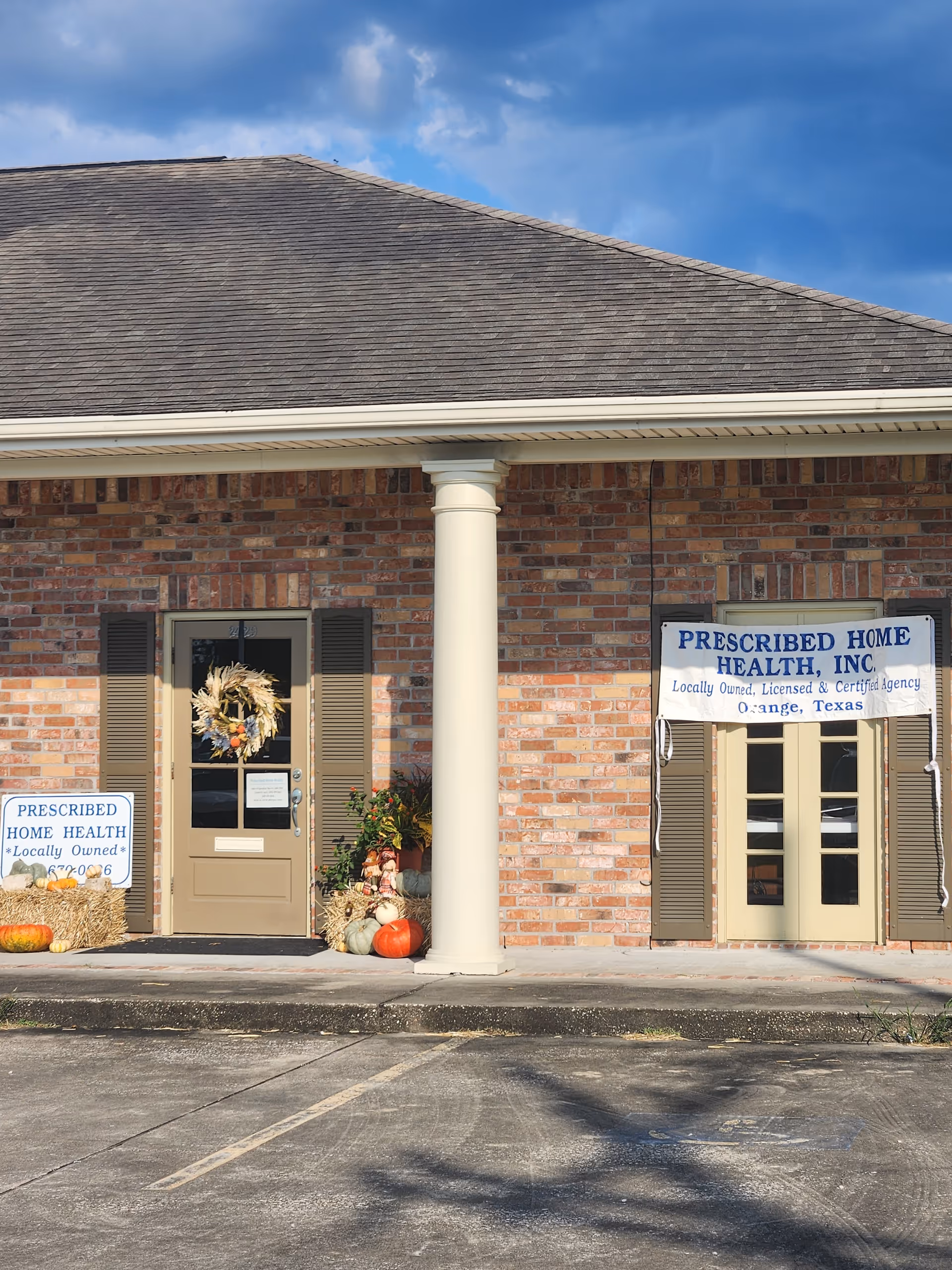 Brick facility front with columned entrance, pumpkins, wreaths, and signage for Prescribed Home Health.