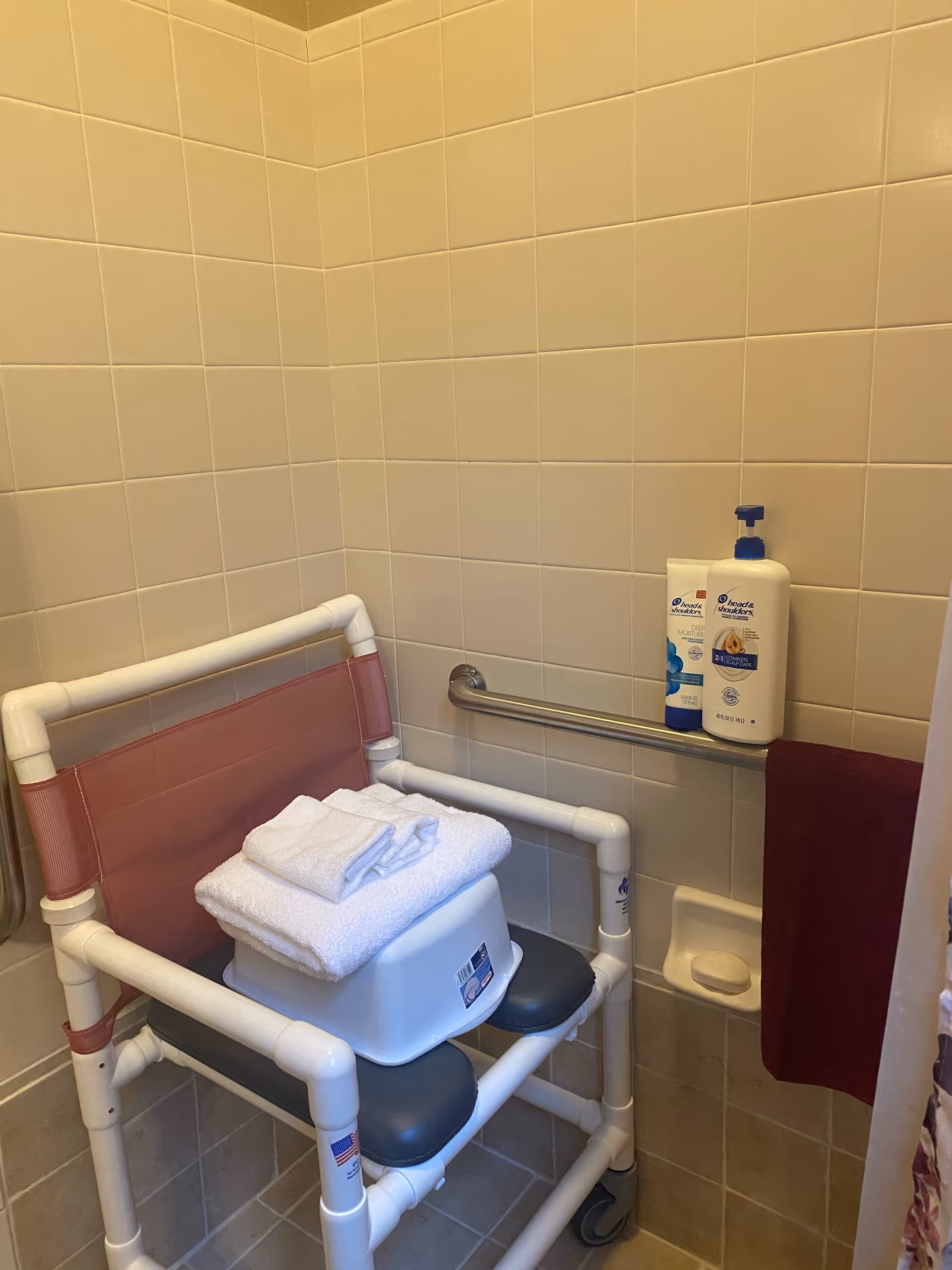 Accessible bathroom with a wheeled shower chair, grab bar, and towels.